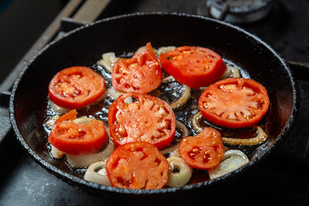 Tomatoes and onions are fried in a pan in boiling oil. Horizontal photo.の写真素材