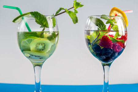 cocktail berry two glasses raspberries blueberries lemon and mint and ivy lime mint in a glass with a straw on a white background. horizontal photoの写真素材