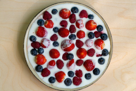 In a plate with whipped cream, ripe berries strawberries, raspberries and blueberries on a light background. horizontal photoの写真素材