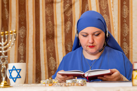 A Jewish teacher woman at a table wearing headphones conducts an online lesson on prayer. Horizontal...