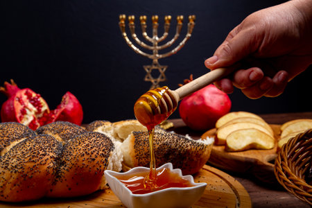 Honey dripping from a spoon on a table in Rosh Hashanah next to an apple challah menorah burning candles. Horizontal photo.の写真素材