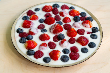 In a plate with whipped cream, strawberries, raspberries and blueberries on a gray table. horizontal photoの写真素材