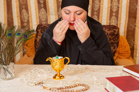 A Muslim woman in a black hijab at a table with incense closes her eyes. Horizontal photo.の写真素材