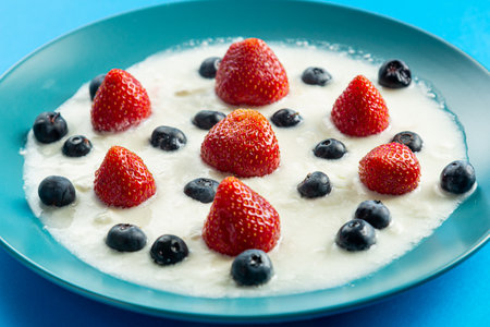 Berries juicy strawberries and blueberries in a blue plate with cream on a blue background. Horizontal photo.の写真素材