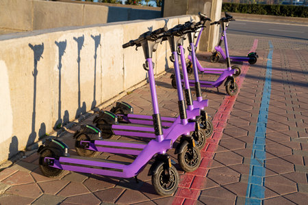 Electric scooters parked on the sidewalk lined up in a row. Horizontal photo.