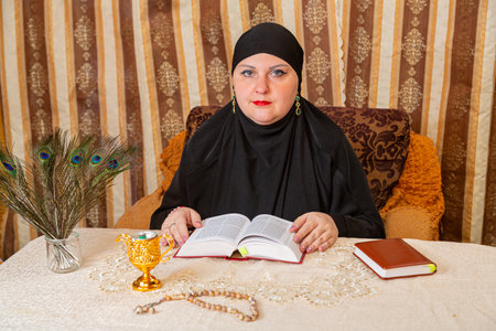A Muslim woman in a black hijab at a table gives women lessons from the Koran. Horizontal photo.の写真素材