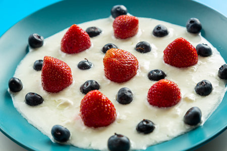 Fresh juicy berries strawberries and blueberries in a blue plate with whipped cream. Horizontal photo.の写真素材