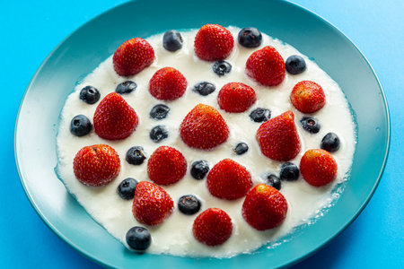 Strawberries and blueberries in a blue plate with cream on a blue background. Horizontal photo.の写真素材