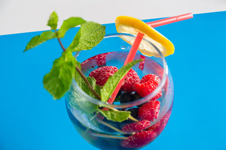 cocktail raspberries blueberries lemon and mint in a glass with a straw on a blue background top view. horizontal photoの写真素材