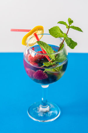 Non-alcoholic cocktail raspberries blueberries lemon and mint in a glass with a straw on a blue background. Vertical photoの写真素材