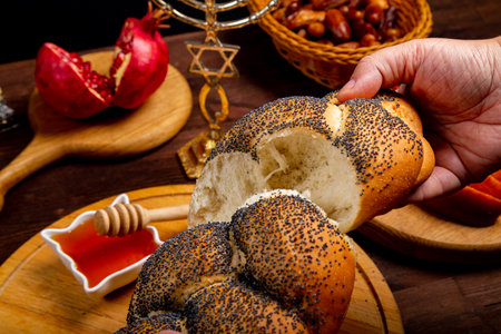 Female hands breaking challah on the table meal in Rosh Hashanah next to apple honey menorah burning candles. Horizontal photo.の写真素材