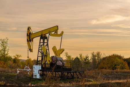 Oil well drilling rig in the middle of autumn field on a clear evening sunset clouds. Horizontal photo.の写真素材