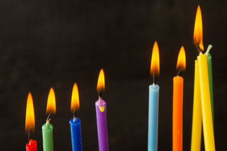 Colored Hanukkah candles burn on the holiday on a black background. Horizontal photo.の写真素材
