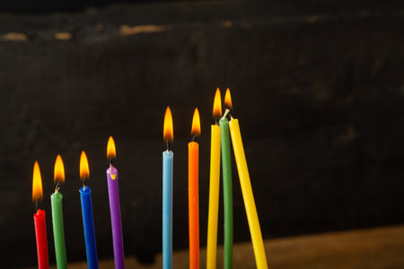 Colored Hanukkah candles burn illuminating darkness on black background. Horizontal photo.の写真素材