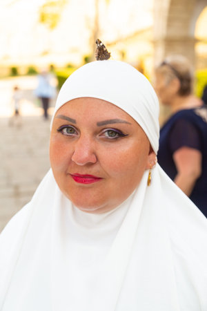 A bright butterfly sits on the head of a Muslim woman in white. Vertical photo.の写真素材