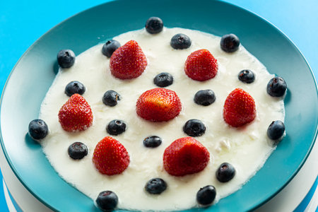 Fresh berries strawberries and blueberries in a blue plate with whipped cream on a blue background. Horizontal photo.の写真素材