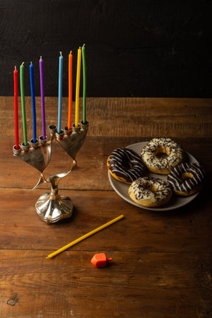 Hanukkiah with colored candles on the table and chocolate glazed donuts and dreidel. Vertical photo.の写真素材