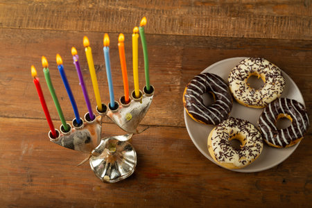 Hanukkiah with colored candles on the table and glazed donuts and dreidel. Horizontal photo.の写真素材