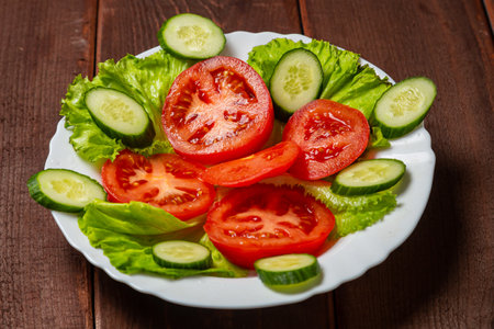 Salad, cucumbers and tomatoes in circles in a white plate on a wooden table. horizontal photoの写真素材