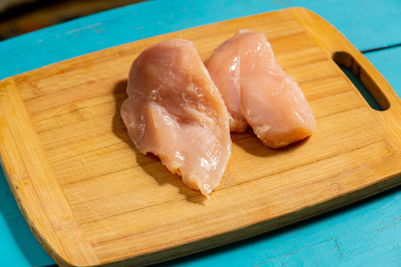 Chicken fillet lies on a wooden board on a blue table. Horizontal photo.の写真素材