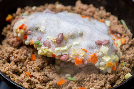 Frozen ground beef is fried in a frying pan with vegetable oil and frozen vegetables.の写真素材