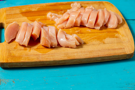 Sliced chicken fillet lies on a wooden board on a blue table. Horizontal photo.の写真素材
