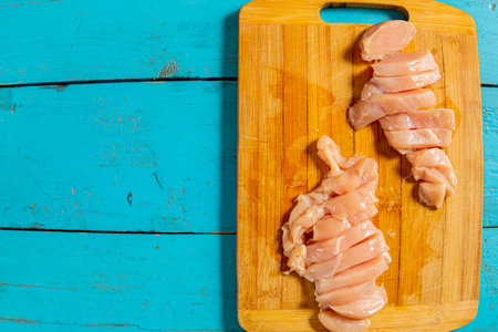 Sliced chicken fillet lies on a wooden board on a blue table. Copy space. Horizontal photo.の写真素材