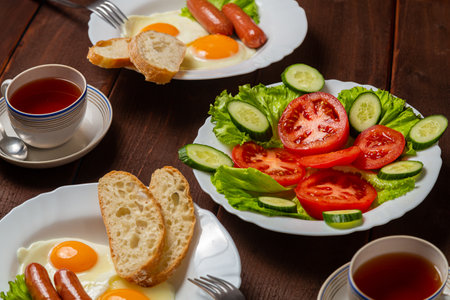 Breakfast two plates of scrambled eggs with chanterelles and white bread, tomato salad and tea in cups. Horizontal photo.の写真素材