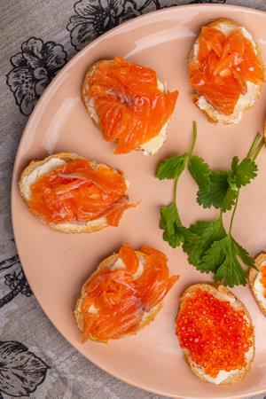 Canapes with red caviar and salted salmon on a plate decorated with cilantro close-up. Vertical...