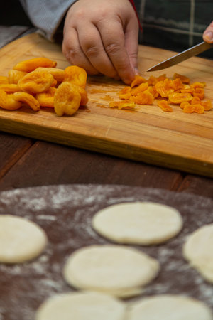 Jewish woman makes a filling of dried fruits and poppy seeds for baking on a wooden table on a round...