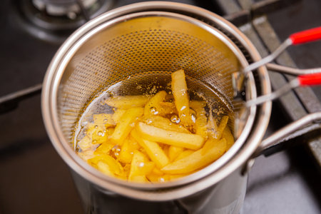 French fries in boiling oil in a deep fryer are cooked on a stove in a home kitchen. Horizontal...