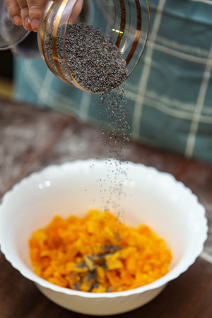 Hands of a Jewish woman pour poppy seeds into the filling of apricots on gomentashi for the holiday of Purim. Vertical photo.の写真素材