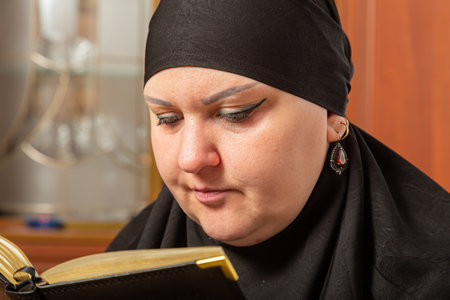 Muslim woman in black hijab reading Quran before prayer close-up. Horizontal photo.の写真素材