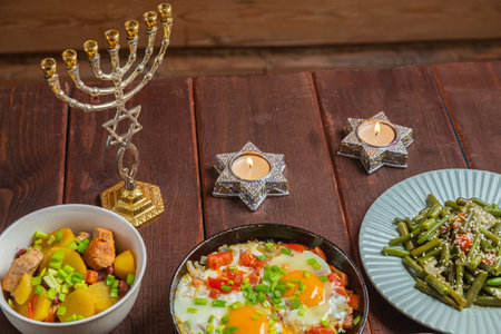 Set table, Jewish food, tzimmes, chelnt, shakshuka and couscous with dried fruits for the holiday with a menorah and candles. Horizontal photo.の写真素材