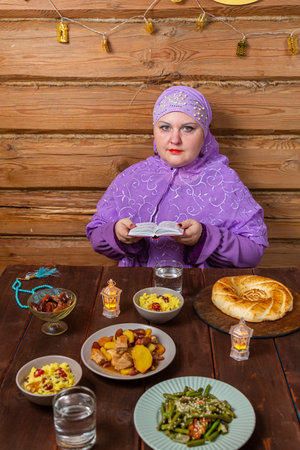 Muslim woman in purple hijab reads dua at festive table Eid al-Fitr Raza Bayram. Vertical photo.の写真素材