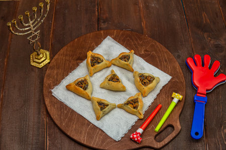 Sweet triangular gomentashi ears of aman for the holiday of Purim on the table, a rattle and a menorah. Horizontal photo.の写真素材