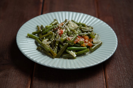 Tzimmes with green beans and tomatoes sprinkled with sesame seeds dish in a plate on the table. Horizontal photo.の写真素材