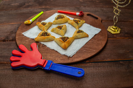 Sweet triangular gomentashi ears of aman for the holiday of Purim on the table, a rattle and a menorah. Horizontal photo.の写真素材