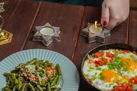 A Jewish woman lights Shabbat candles at a festive table. Horizontal photo.の写真素材