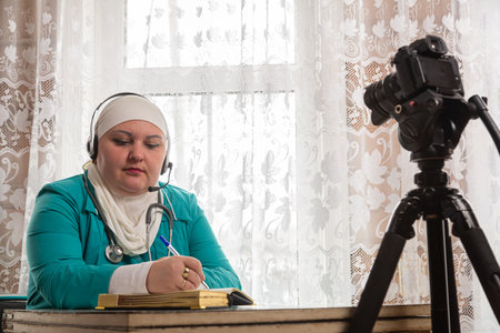 Muslim doctor in white hijab conducts online telemedicine reception from home. Horizontal photo.の写真素材