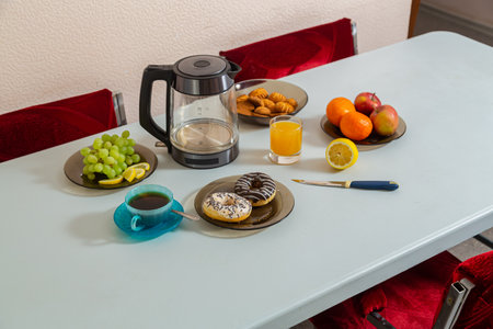 The dining table on it has fruits, juice, cakes, tea, and a horizontal photo.