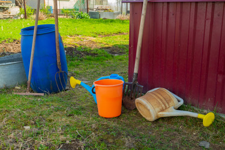 Garden buckets and watering cans of different colors in a suburban area near the wall of the houseの写真素材