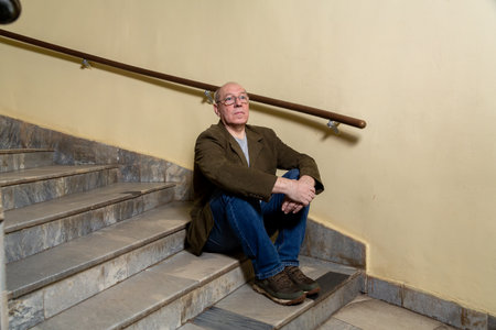 A middle-aged man in a green jacket sits on the steps of a semicircular staircase. Horizontal photo.の写真素材