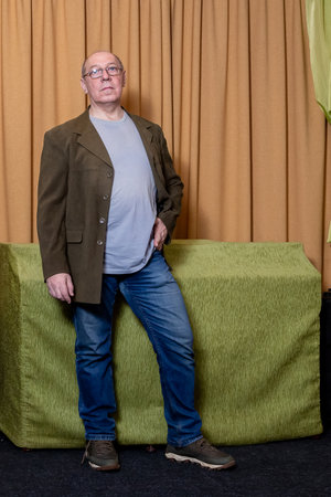 A middle-aged man in a brown jacket near a orange curtain. Vertical photo.の写真素材
