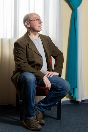 Middle aged man in green jacket beautiful curtain on window. Vertical photo.の写真素材