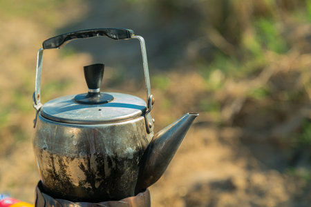 A small metal kettle is boiling on a camping gas burner in nature. Vertical photoの写真素材