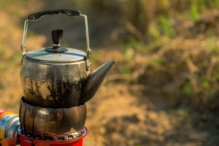A small metal kettle is boiling on a camping gas burner in nature. Vertical photoの写真素材