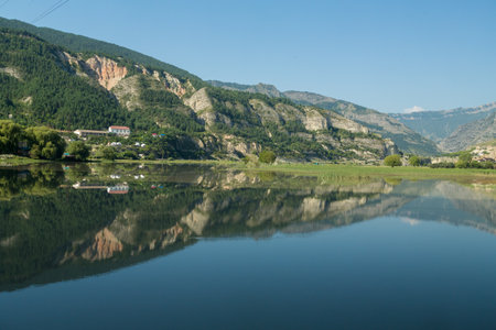 Mountain lake is not large near steep cliffs, mirror-like on a sunny morning. Horizontal photo.の写真素材