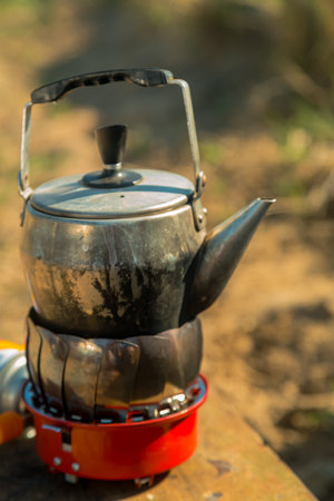 A metal kettle is boiled on a camping gas burner in nature. Vertical photoの写真素材