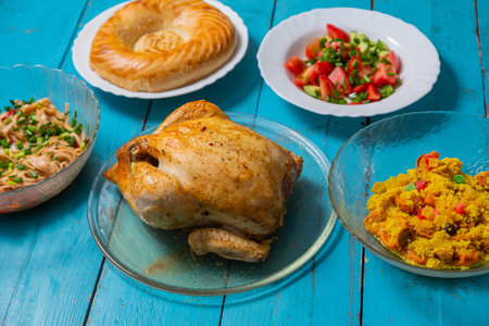 Couscous with dried hands and turmeric, grilled whole chicken, flatbread, and vegetable salad on a blue wooden table. Horizontal photo.の写真素材